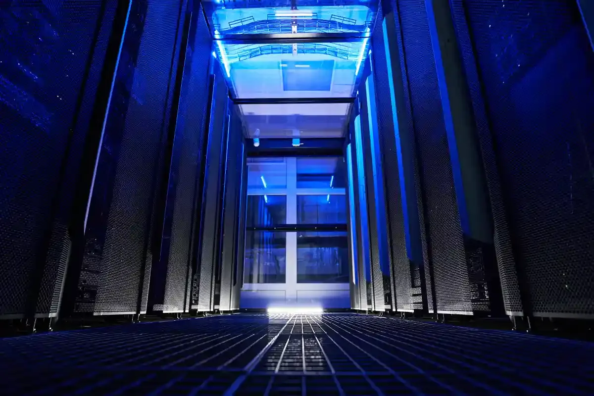 A row of server racks at night in a data center, lit in a blue color.